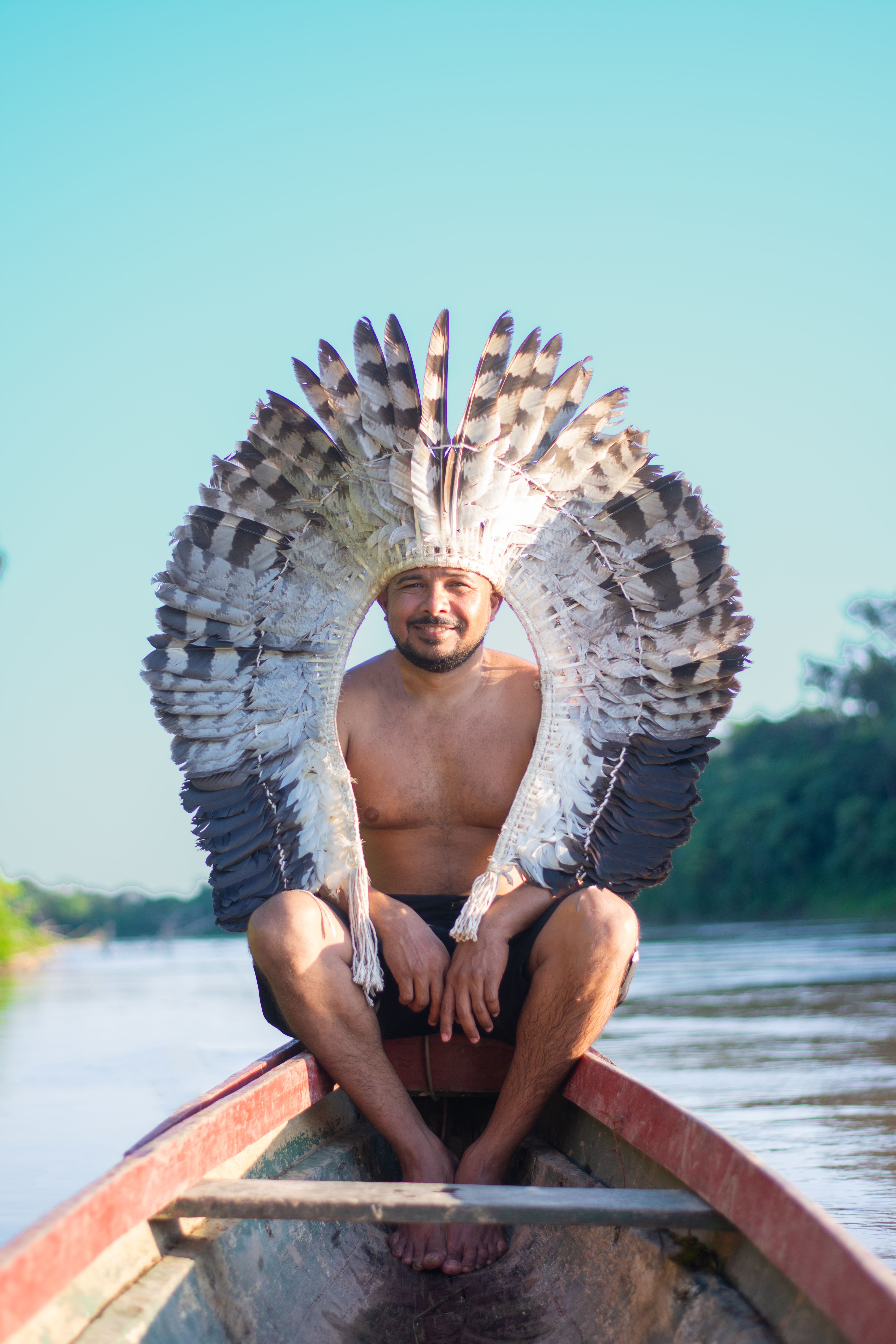 Liderança indígena segurando cocar tradicional na canoa em águas amazônicas